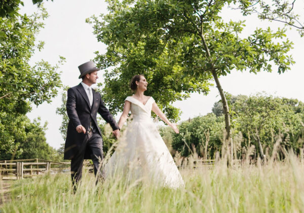 Couple in the apple orchards holding hands next to wedding car at La Mare Wine Estate