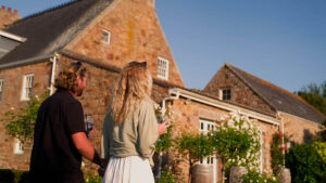 Couple strolling through the gardens at La Mare Wine Estate with Jersey granite farmhouse in the background