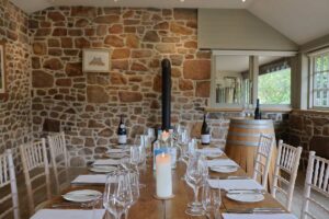 A big table laid out for dinner with glasses and plates and candles and bottles of wine. 